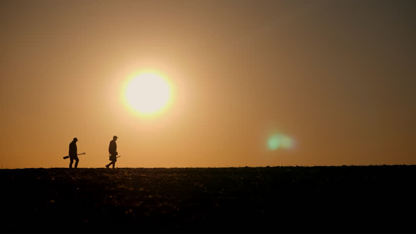 Two farmers walking across a field at sunrise or sunset, silhouetted against the glowing sun. The scene highlights the simplicity and connection to nature in rural life 