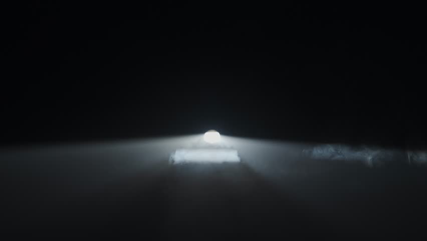 Bright white spotlights rays of professional lighting equipment flashing in darkness on right side of frame, green smoke moving through the light.