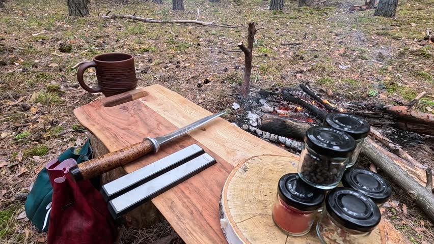 A man sharpens a knife outdoors by a campfire