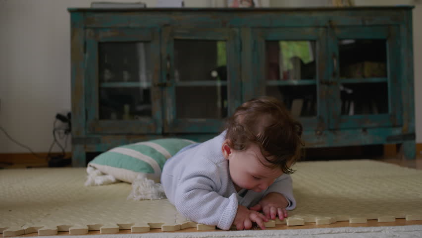 Baby lying on mat, touching and exploring textured objects with hands, focused on tactile engagement and sensory development in a calm home environment