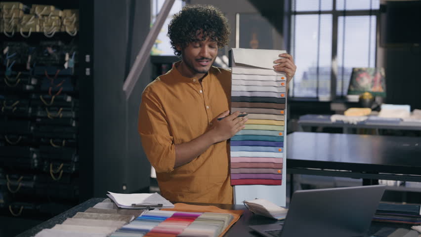 Arabian Indian man guy male fashion designer tailor stylist decorator salesman presenting samples color palette cloth fabrics talking video call online laptop conference offer client in textile shop