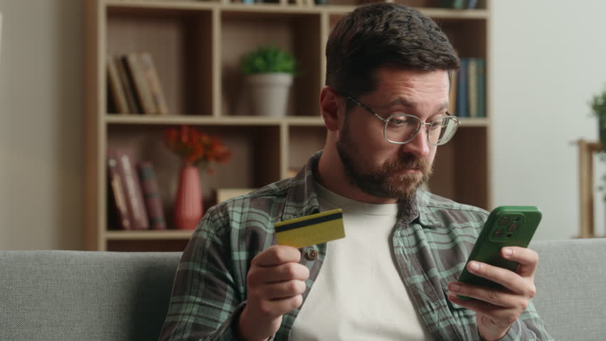 Confused puzzled angry Caucasian man male guy buying shopping online mobile phone smartphone buying purchase problem failure blocked credit bank card trouble scam error internet payment money at home