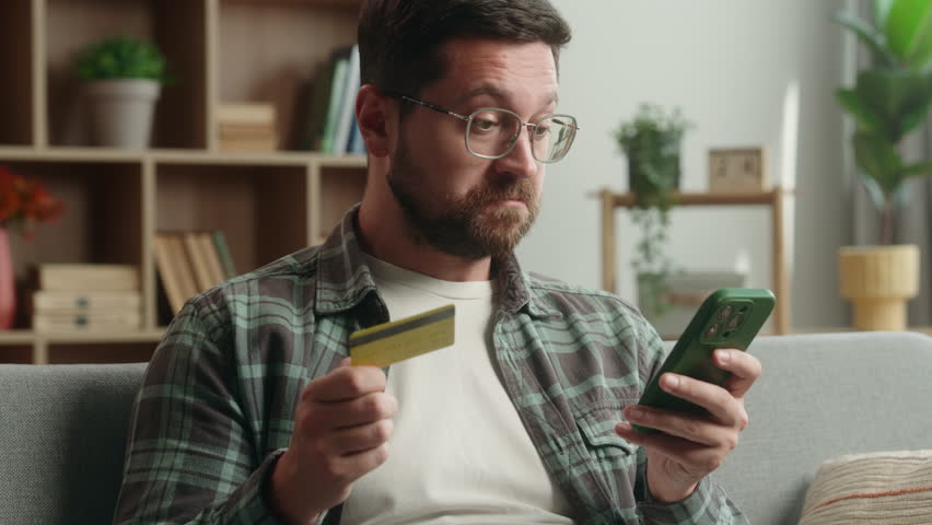 Confused puzzled angry Caucasian man male guy buying shopping online mobile phone smartphone buying purchase problem failure blocked credit bank card trouble scam error internet payment money at home