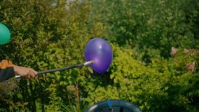 Purple balloon floats in garden setting as it meets flaming torch, causing explosive burst of vibrant orange flames. Intense contrast between the balloon’s color and the bright fire - Powered by Shutterstock - Get 15% off with code: PIKWIZARD15