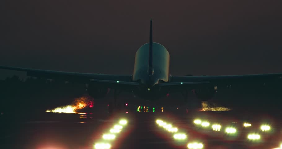 A passenger plane lands on the illuminated runway of the airport at night. Slow motion video of an airliner arriving at the airport. High quality 4k footage