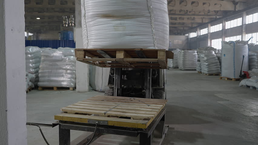 Using a forklift to lower down a huge bag on a pallet inside a warehouse. Industrial forklift handling heavy pallets at a warehouse. Forklift putting down pallet with a heavy container at warehouse. - Powered by Shutterstock - Get 15% off with code: PIKWIZARD15