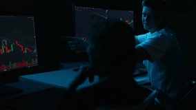 Male and female stock market traders discussing candlestick charts displayed on multiple computer monitors in dark room, analyzing market trends, making investment decisions. Shooting in slow motion. - Powered by Shutterstock - Get 15% off with code: PIKWIZARD15