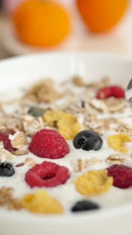 Vertical: the spoon takes fresh milk yogurt from the bowl along with the berry of raspberries and blueberries with the addition of natural granol and oats and corn flakes. Healthy healthy breakfast