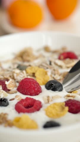 Vertical: the spoon takes fresh milk yogurt from the bowl along with the berry of raspberries and blueberries with the addition of natural granol and oats and corn flakes. Healthy healthy breakfast