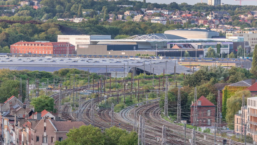 Aerial timelapse of Brussels North station curved railway tracks with trains arriving and departing. Schaerbeek cityscape featuring depot, shopping mall and industrial areas with solar panels. Belgium