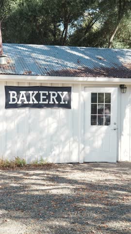 general shot of small bakery in a history town of Columbia, young lady wearing a poncho is leaving the bakery with a coffee in her hands, 4k video vertical