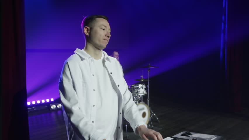 Two musicians in white outfits are performing on stage. The keyboard player is rocking out while the drummer plays the drums energetically