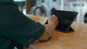Woman engages with tablet while in laundromat, blend of technology and everyday tasks, highlighting convenience in managing laundry with digital tools - Powered by Shutterstock - Get 15% off with code: PIKWIZARD15
