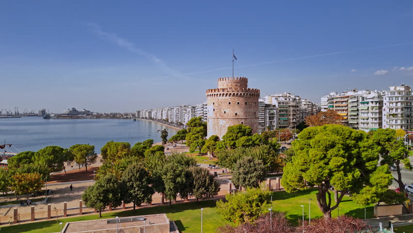 This stunning aerial perspective showcases the iconic White Tower of Thessaloniki, surrounded by lush greenery and the waterfront along the serene sea.