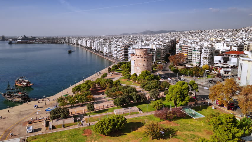 Captivating aerial view of Thessaloniki highlighting the waterfront, historical White Tower, and vibrant coastal activities under a clear sky during daytime.