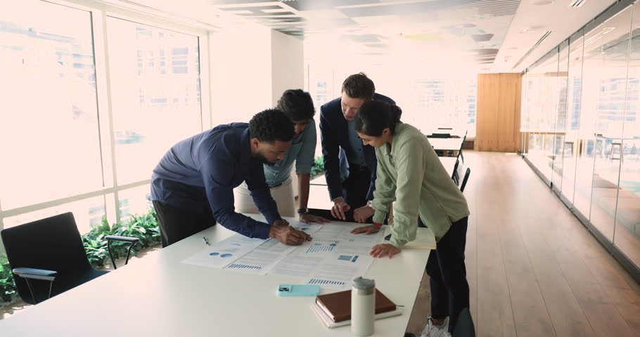 International team celebrating success with high five over project roadmap. Diverse professionals collaborate on strategy solution, discussing ideas, paperwork for business growth, motivated teamwork