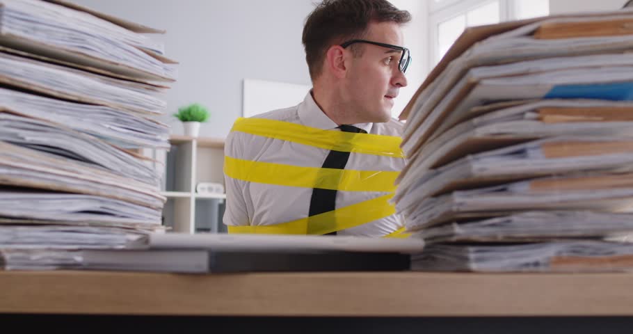 Office slave stuck at work. Funny bookkeeper tries to escape from workplace. Man who is glued to chair with scotch tape by desk with piles of paperwork cautiously looks around and starts his way out