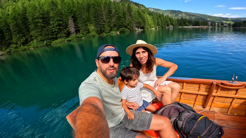 Happy family with a child taking a selfie while enjoying a boat trip on the beautiful lake braies in the dolomites, italy, during summer