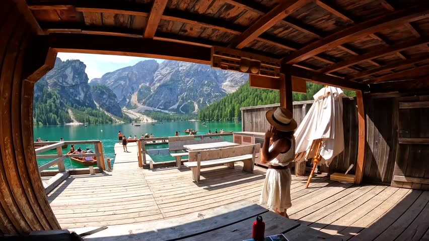 Woman wearing straw hat enjoying stunning panorama of lake braies, also known as pragser wildsee, in the heart of the dolomites, a unesco world heritage site