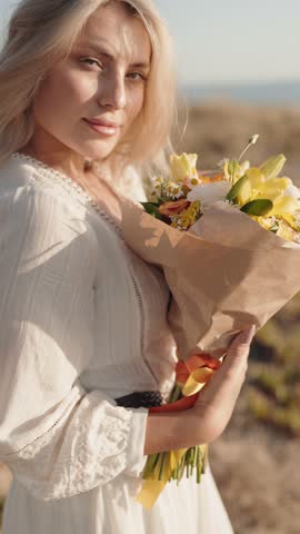 Close up of a beautiful young blonde woman holding a bouquet of flowers and smiling. She is joyful.