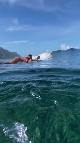 Two young female surfers making duck dive in the ocean, Indonesia