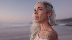 A thoughtful mature woman with gray hair and a tattoo reflects on life's journey while enjoying a peaceful sunset at the beach. - Powered by Shutterstock - Get 15% off with code: PIKWIZARD15