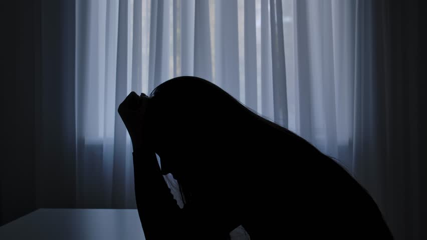 Silhouette of woman sitting at table in front of window, begging regretting expression, sad heartbroken mood, painful tired face. Human emotions and mental health.