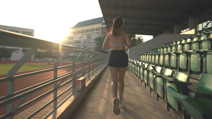 A woman runs on a track with a green fence in the background. Concept of determination and focus as the woman pushes herself to complete her run