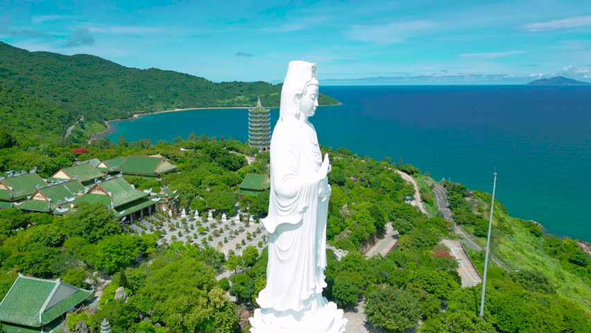 The majestic Lady Buddha statue overlooks lush greenery and serene waters, embodying spiritual tranquility in Da Nang's landscape.