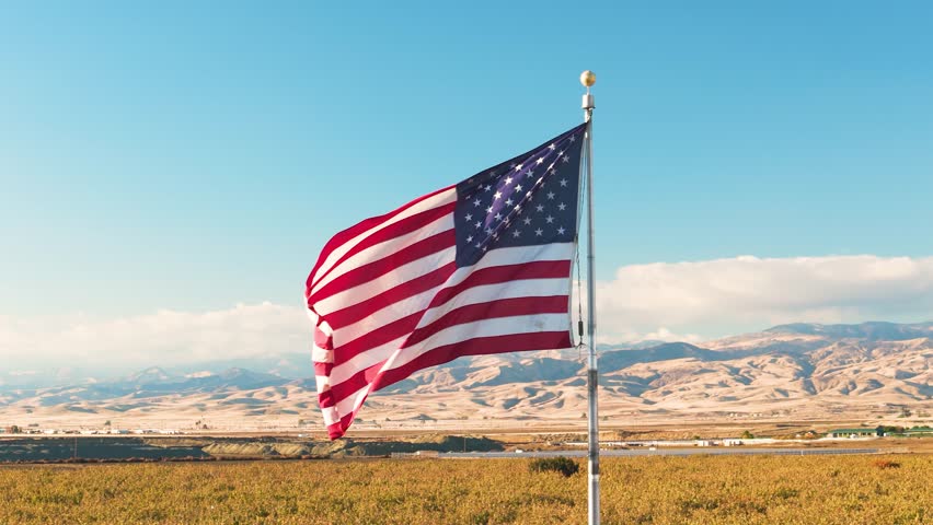 American Flag Waving in Wind, Patriotic Symbol Against Blue Sky and Mountains