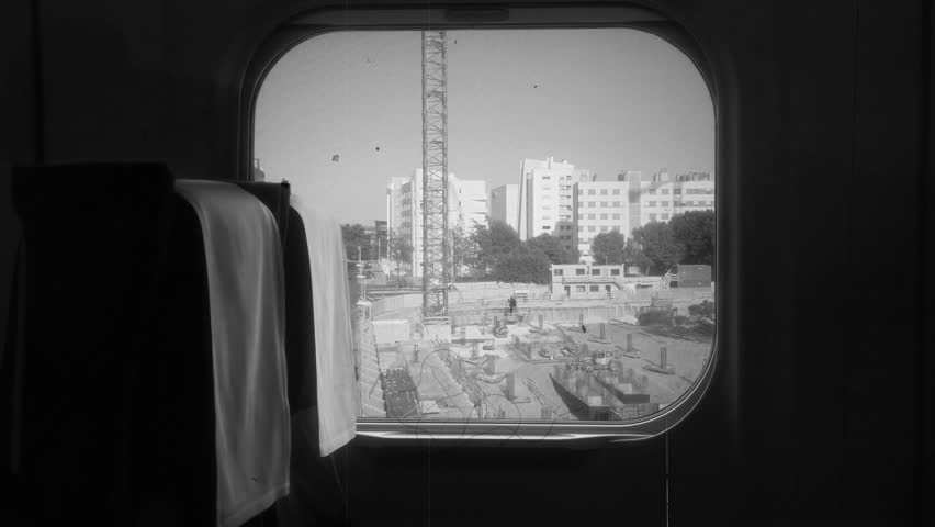 Train Travel Vintage Window View City Buildings Vehicle Shot Old Film Effect. A black and white photograph captures an urban construction site viewed through a train window,.