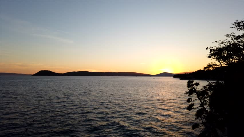 Motionlapse pan right of sunset over the Adriatic Sea near Croatia, with changing hues and calm water as boats return to harbor