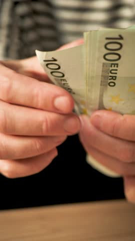 Vertical: White woman's hands holding euro banknotes counting the amount of money by hand. Woman counting euro cash after receiving unemployment benefit or salary