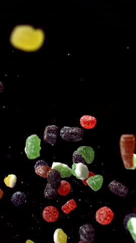 An assortment of brightly colored, sugar-coated jelly candies gently tumbles through the air, beautifully highlighted against a deep black backdrop