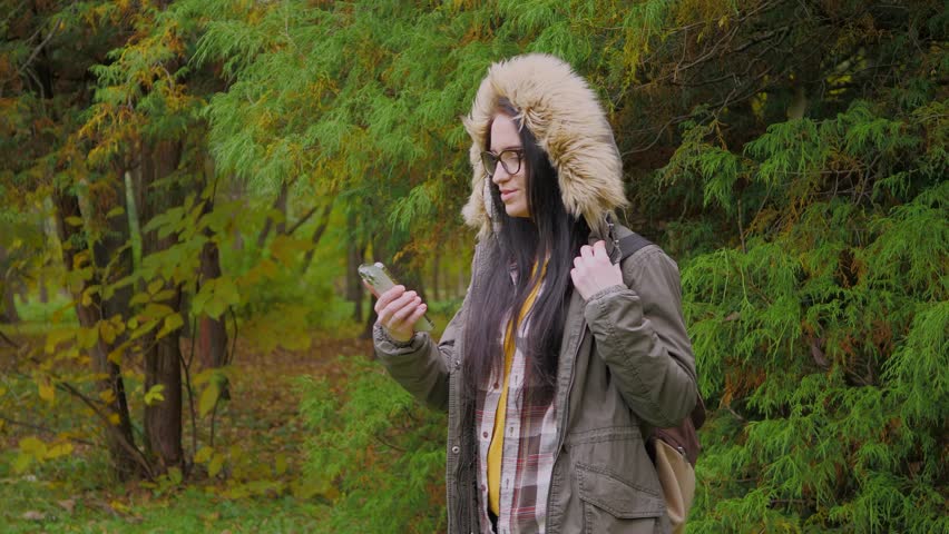 Travel in nature. A young beautiful girl in an autumn forest enjoys the beauty of autumn nature, walks, communicates with the autumn beauty of the forest, holds a drink in a glass in her hands, smiles