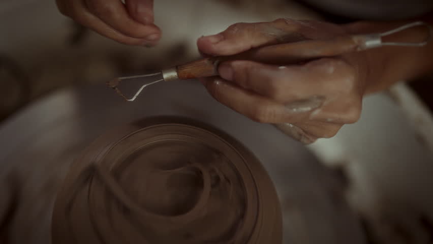 Close-up of an artisan's hands carefully using a loop tool to shape the foot of a pottery piece on the potters wheel