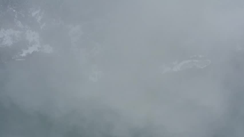 Drone footage: a river flowing at the foot of a snow-covered mountain covered in deep fog