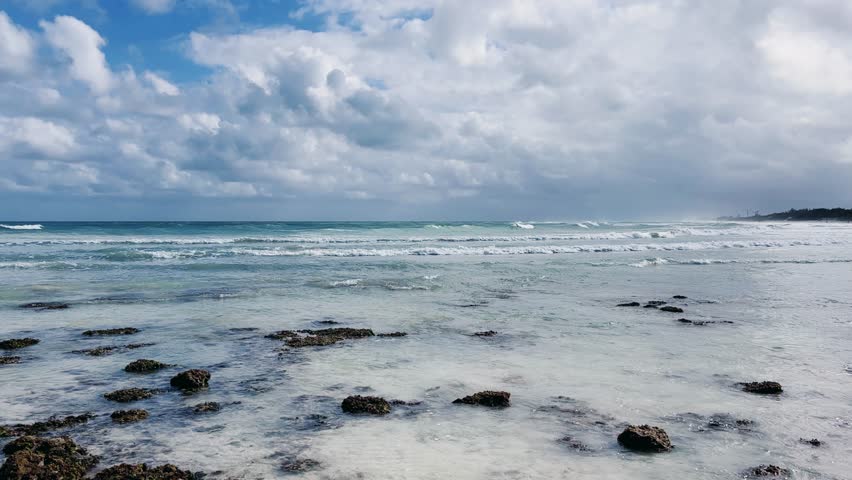 Rocky Cuban beach in Varadero, Cuba, on a cloudy day, when the sun breaks through the clouds, you can see the waves and ocean expanses. Turquoise waves. Stone slabs on the beach in the ocean. 4K	