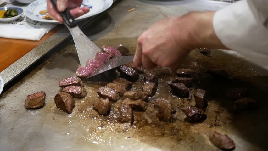 Japanese chef slicing wagyu Kobe beef steak juicy meat while grilling meat in a grill at a japanese restaurant prepared to served marble beef tepanyaki cooking Japanese style