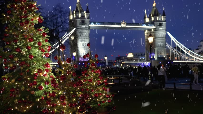 A beautiful Christmas Tree in front of the defocussed Tower Bridge of London, England, with snow falling during winter evening time