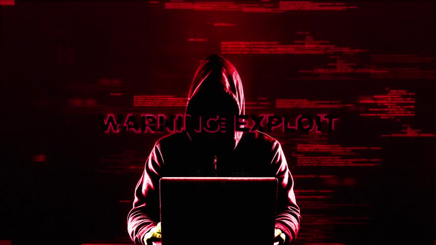 A hooded figure uses a laptop against a background of red code, warning of a cybersecurity exploit.