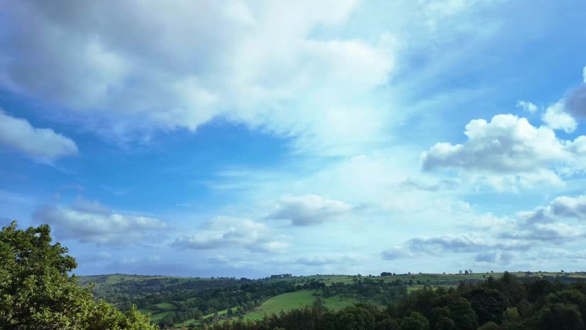 A timelapse of white clouds moving in a bright, blue sky over an English countryside landscape