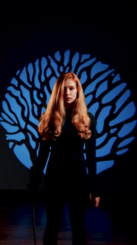 Red-haired woman posing with a katana against the backdrop of a light tree. Portrait of a woman with a samurai sword. Japanese culture concept. Vertical 4k video