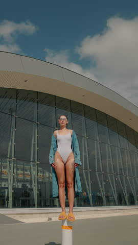 Stylish Model In White Swimsuit On Background Of Modern Oval Building.