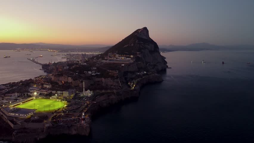 Aerial view of Gibraltar at sunset. Street lights on. Europa Sports Complex Stadium with night light on. Famous travel destination. Bay of Gibraltar. City of Gibraltar and La Linea, in background.