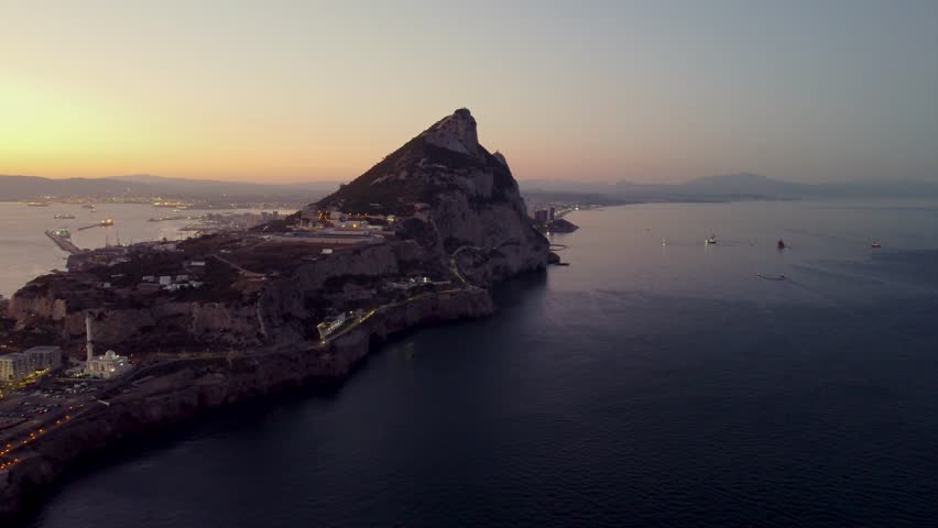 Aerial view of Gibraltar at sunset. Street lights on. Europa Sports Complex Stadium with night light on. Travel destination. Bay of Gibraltar. City of Gibraltar and La Linea, in background. Track left