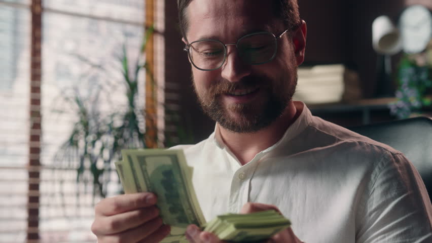 Glad Caucasian man boss accountant guy entrepreneur smiling count stack of money cash dollars payment banknotes business receiving salary male worker businessman calculating financial budget in office