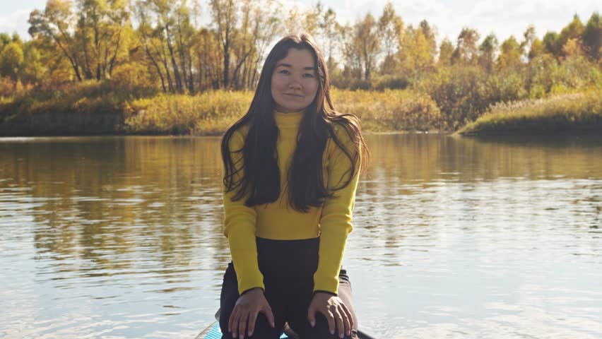 Young and attractive woman of Asian origin is interested in a unique sport - paddleboarding. She looks straight into camera and smiles.