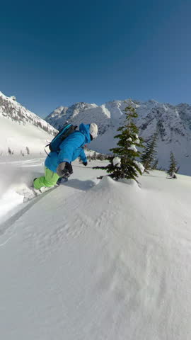SELFIE: Awesome shot of mountains as man snowboards in the breathtaking Canadian backcountry. Extreme snowboarder shreds powder while carving between pine trees. Man heliboarding in British Columbia