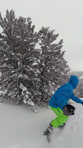 SELFIE: Breathtaking shot of an extreme male snowboarder speeding down the ungroomed slope in the Rocky Mountains. Male tourist shreds fresh powder snow while cat boarding in the mountains of Wyoming.